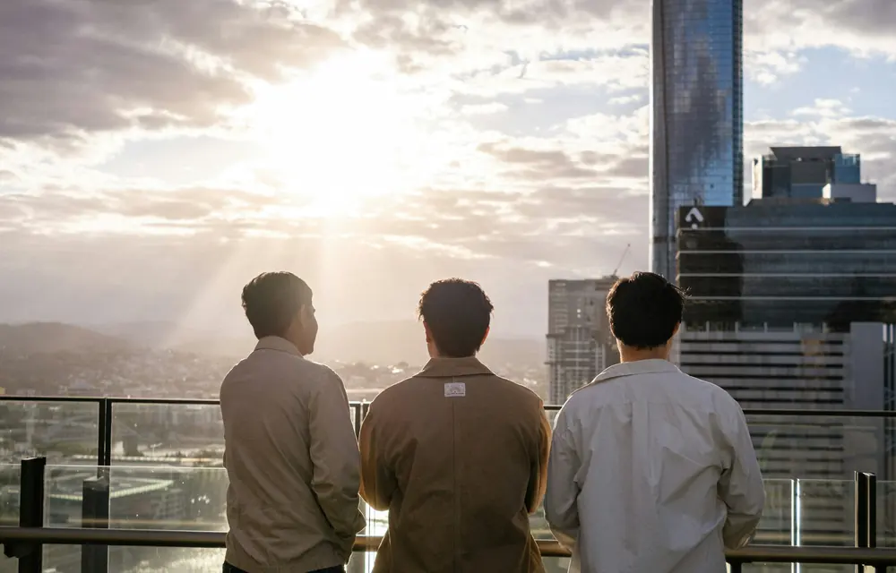 Three travellers standing together looking out over a city skyline at sunset