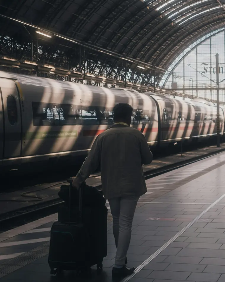 A traveller walking alone along a station platform, pulling their luggage past a waiting train
